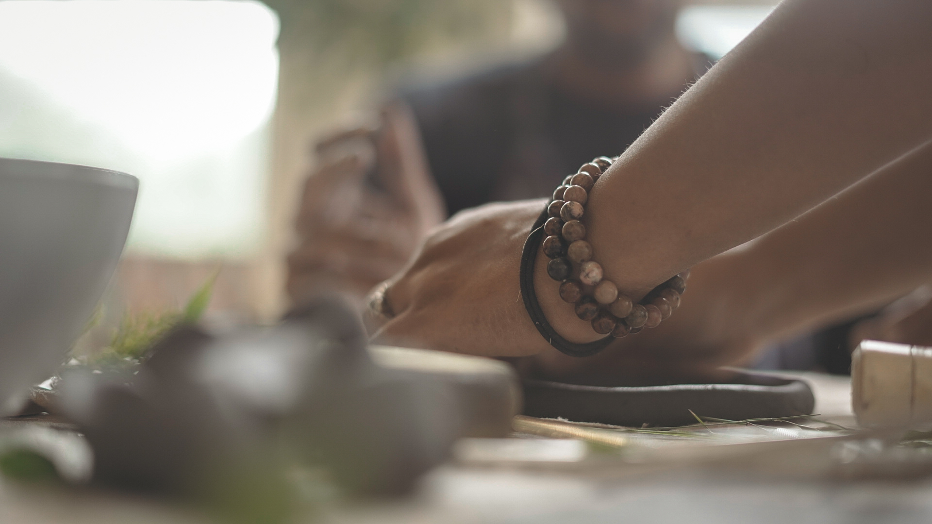Hands pressing clay on a work surface with botanical leaves nearby